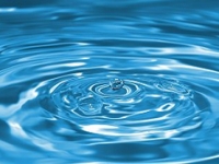 Ein Tropfen Wasser trifft auf eine blaue Wasserfläche.