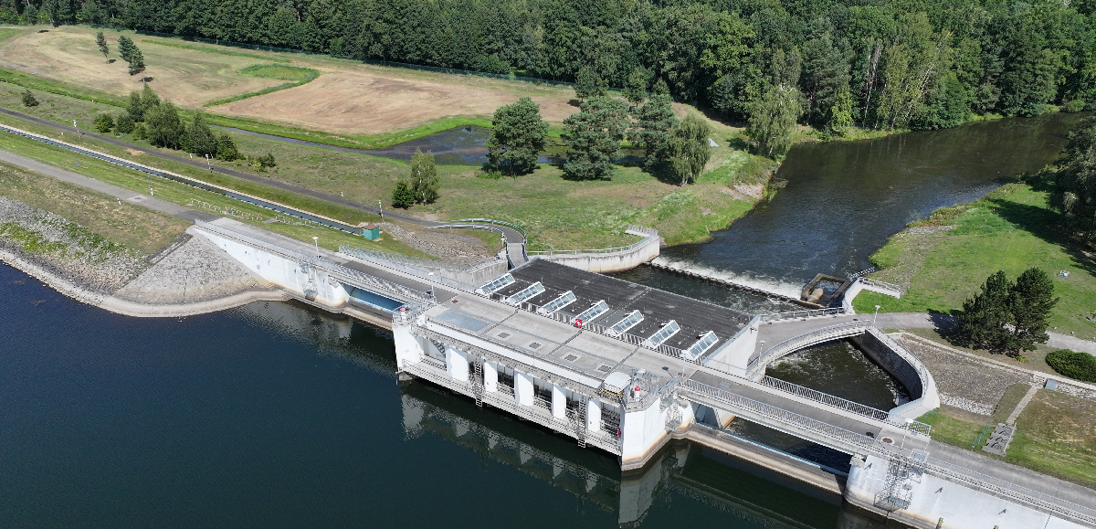 Das Grundablass- und Entlastungsbauwerk der Talsperre Spremberg Luftaufnahme des Grundablass- und Entlastungsbauwerks der Talsperre Spremberg, welches links und rechts von Dämmen gesäumt wird. Die Szene wird dominiert von der massiven, hellgrauen Betonstruktur des Bauwerks, der Vordergrund wird vom tiefdunklen Wasser des Stausees eingenommen. Im Hintergrund sieht man den Lauf der Spree, welcher in ein Waldstück fließt.