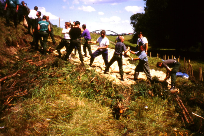 Mehrere Menschen helfen am Kanaldeich Eisenhüttenstadt. Es wird versucht die Böschung mit Sandsäcken zu sichern.